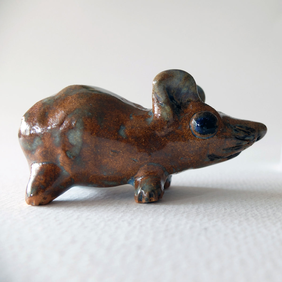 Handcrafted ceramic mouse figurine with a glossy amber-brown glaze, blue accents, and dark eyes, sculpted by Nikolaj Jesper Cyon.