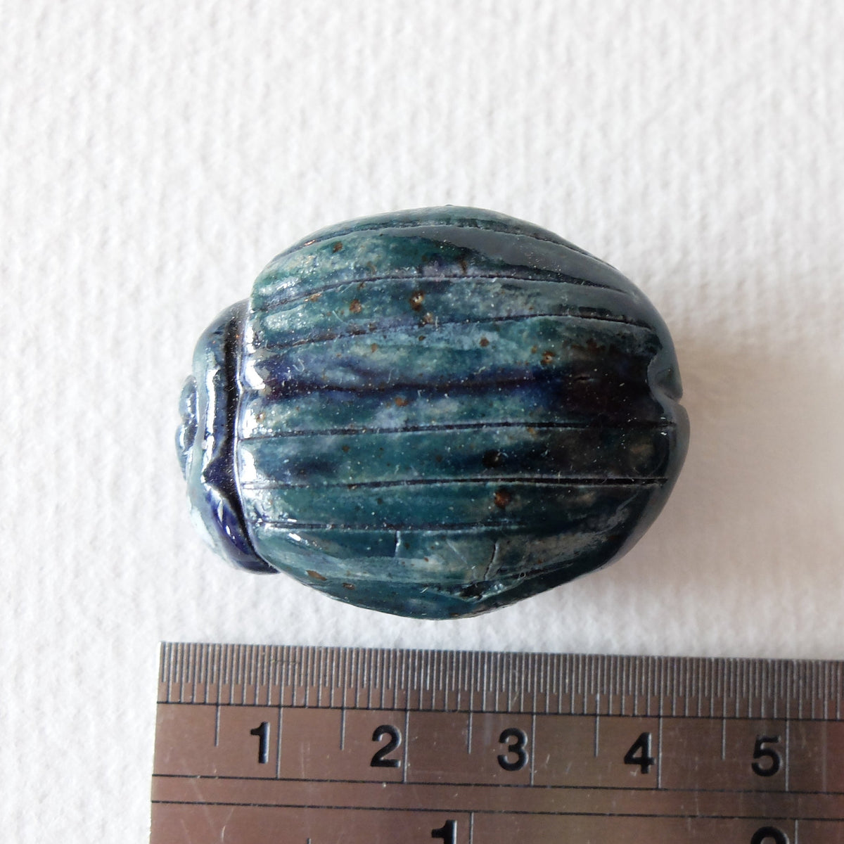 Handcrafted ceramic beetle figurine "The Jade Scarab (#6)" in stoneware by Nikolaj Jesper Cyon. Top-down view next to a metal ruler showing size scale.