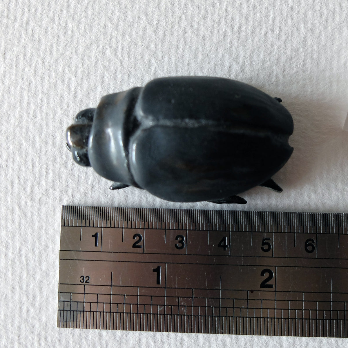 Handcrafted ceramic beetle figurine "The Midnight Beetle (#2)" in stoneware by Nikolaj Jesper Cyon. Top view next to a ruler showing size scale.