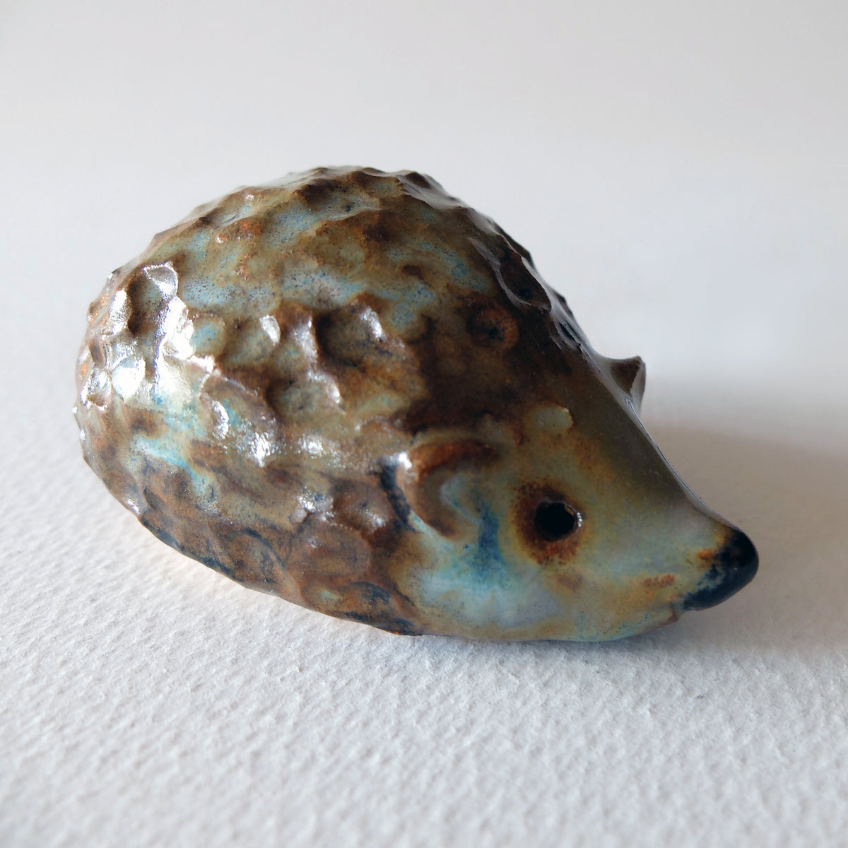 Handcrafted ceramic hedgehog figurine with a knobby textured back in a mottled blue, beige, and green glaze, sculpted by Nikolaj Jesper Cyon.