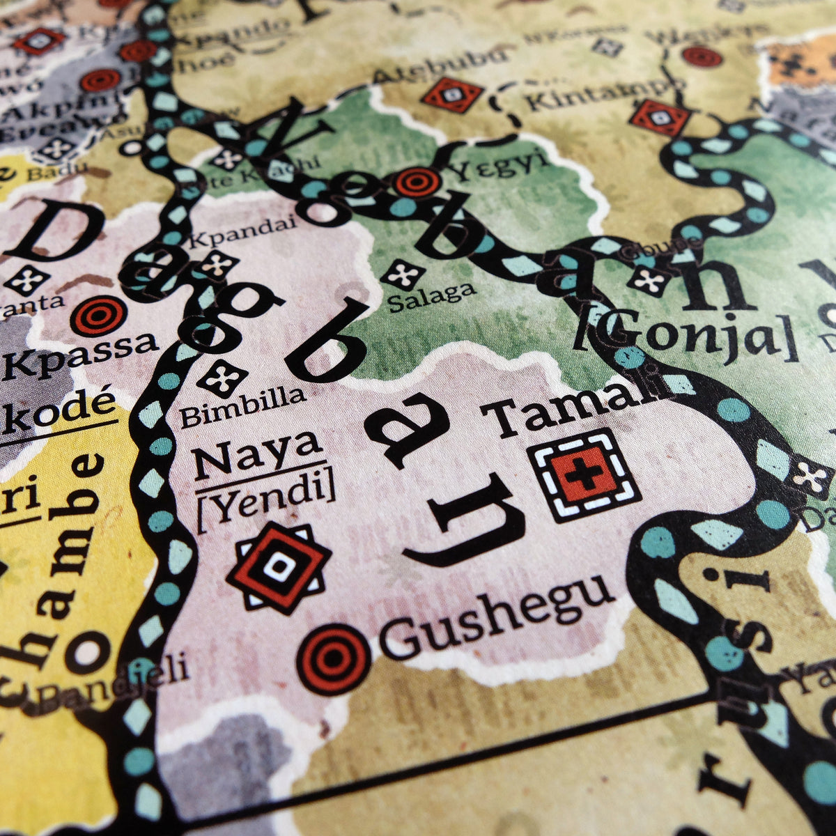 Macro photograph showing the Dagbaŋ realm and surrounding territories on the Alkebu-Lan map print, situated across modern Ghana, Togo, Benin, and Burkina Faso. Features historic trade hubs like Salaga, Yendi [Naya], Tamale, and Bimbilla—key meeting points for Dyula merchants trading kola nuts, gold, salt and other goods, as well as cultural crossroads between Gurunsi, Dagomba, and Ashanti spheres. Printed on textured paper by Nikolaj Jesper Cyon.