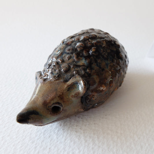 Handcrafted ceramic hedgehog figurine "The Cautious Mulberry Hedgehog (#17)" in stoneware by Nikolaj Jesper Cyon. Features a timid posture with a bumpy, dark brown and charcoal mulberry-textured back and a smooth beige snout.