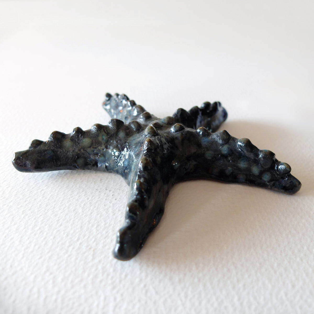 Handcrafted ceramic starfish figurine "The Knobby Starfish (#21)" in stoneware by Nikolaj Jesper Cyon. Five-armed starfish sculpture with bumpy textured surface, finished in glossy dark charcoal and slate glaze.