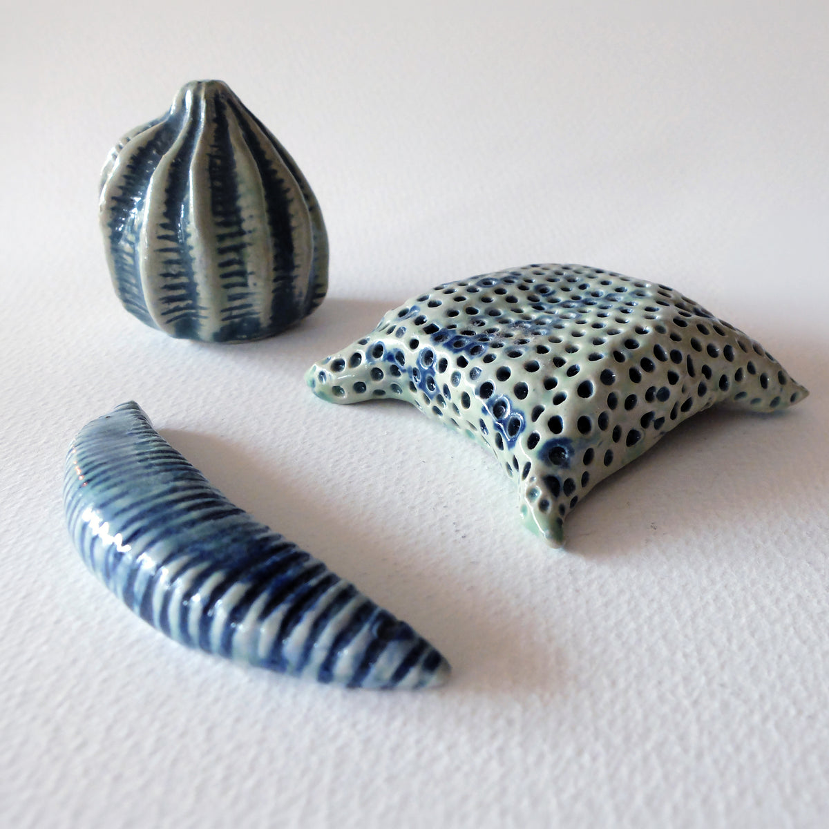 A set of three handcrafted ceramic micro-organism sculptures inspired by diatoms and pollen grains in blue and light green glazes, sculpted by Nikolaj Jesper Cyon.