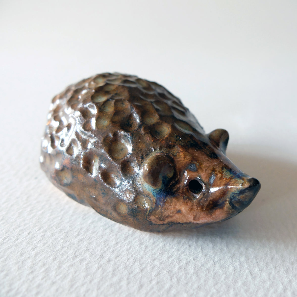 Handcrafted ceramic hedgehog figurine with a knobby textured back in a warm auburn, pinkish-beige, and earthy glaze, sculpted by Nikolaj Jesper Cyon.
