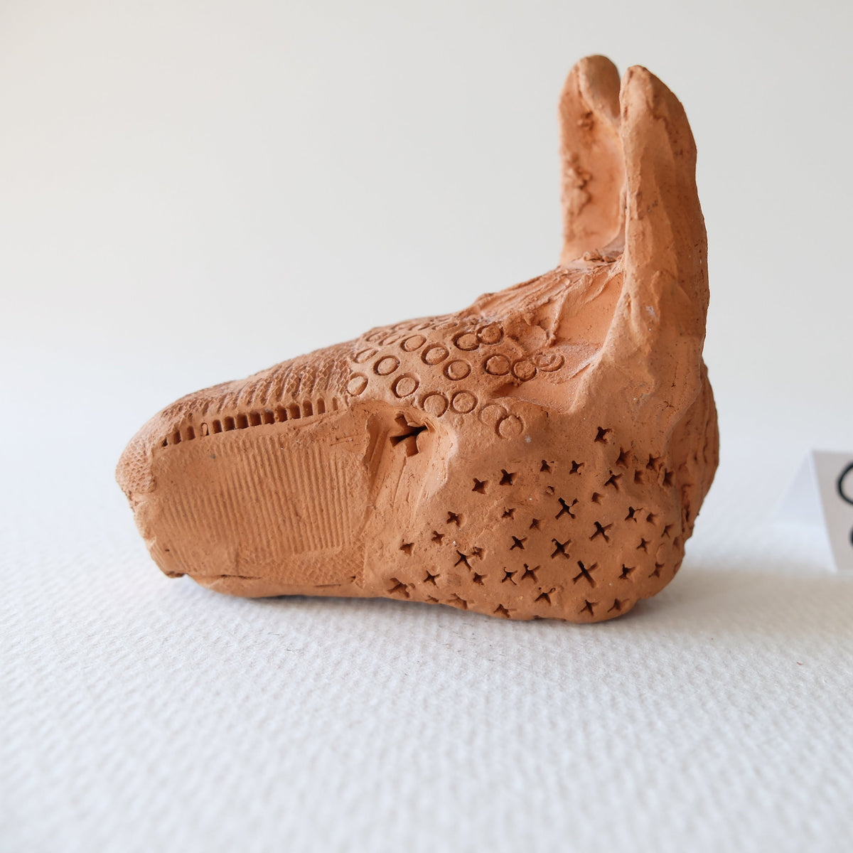 Handcrafted terracotta donkey head sculpture "The Babylonian Donkey (#8)" by Nikolaj Jesper Cyon. Side profile view highlighting the raw, unglazed terracotta clay and stamped geometric surface patterns.
