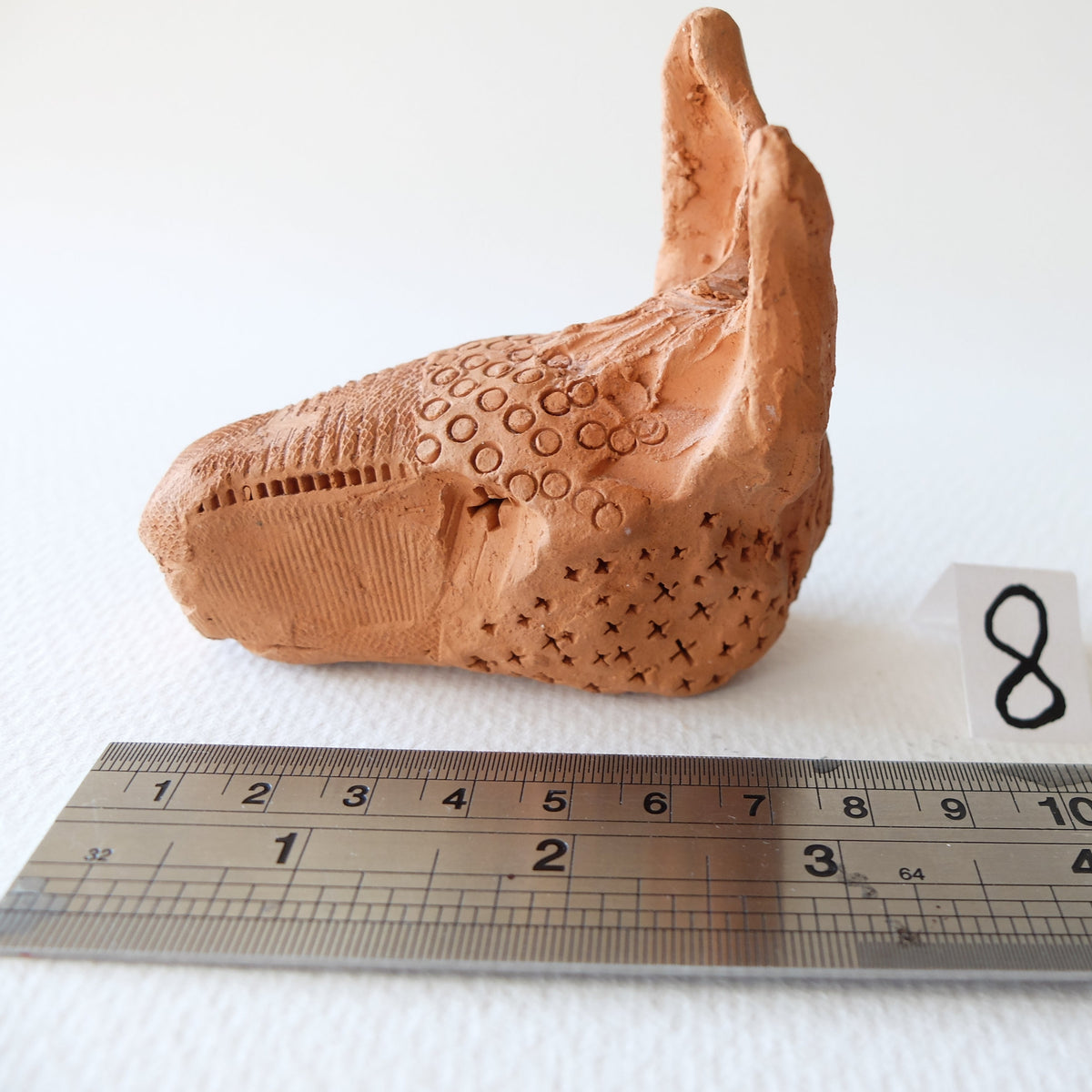 Handcrafted terracotta donkey head sculpture "The Babylonian Donkey (#8)" by Nikolaj Jesper Cyon. Side profile view next to a metal ruler showing size scale.