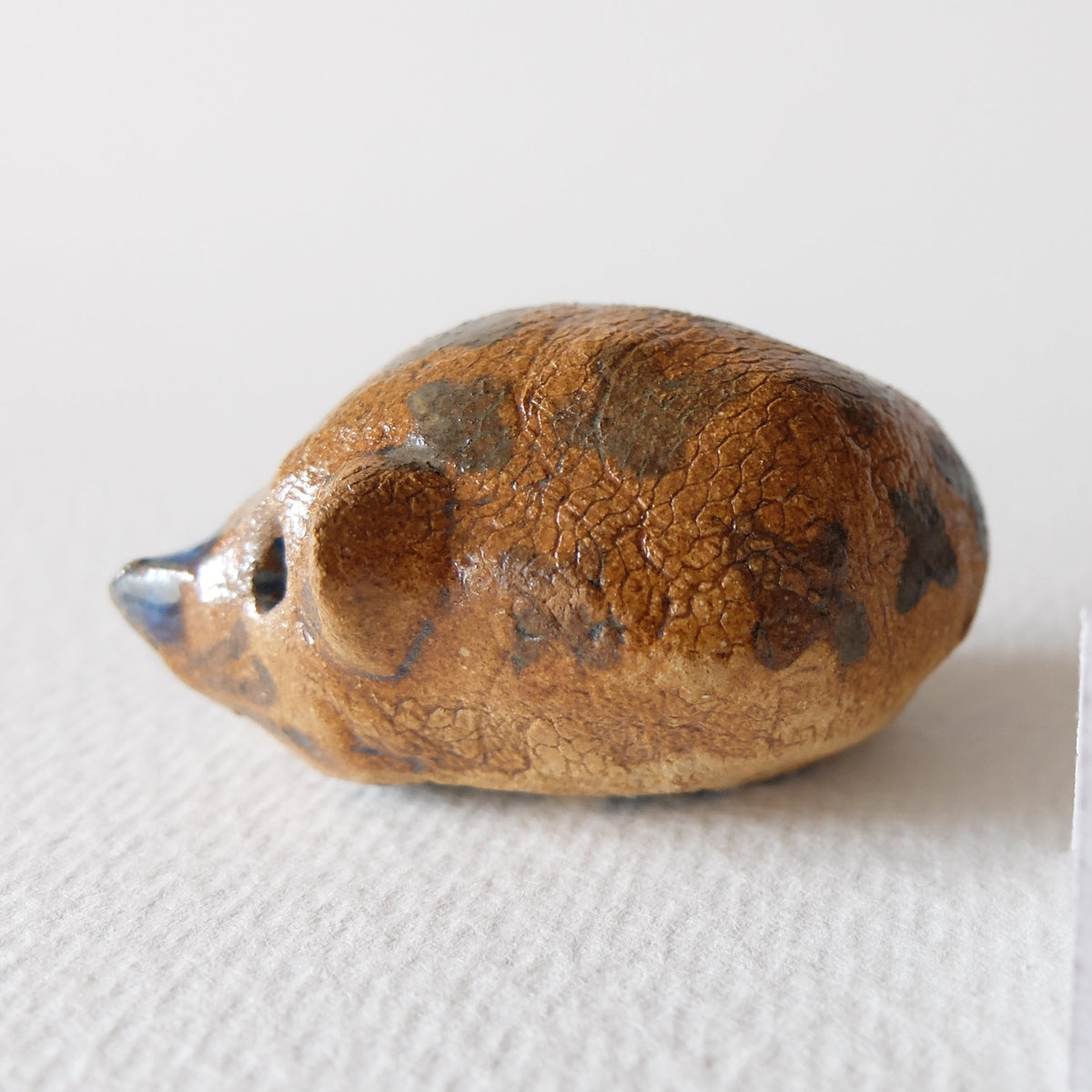 Handcrafted ceramic hedgehog figurine "The Chestnut Hedgehog (#5)" in stoneware by Nikolaj Jesper Cyon. Side profile view showing warm, earthy chestnut brown glaze tones.