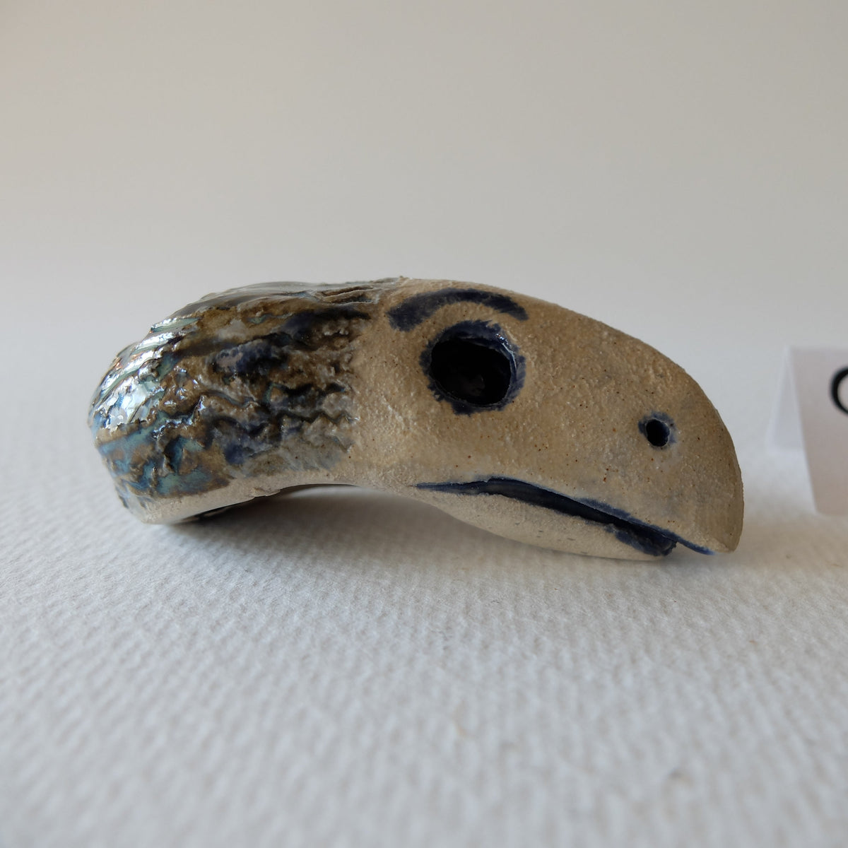 Handcrafted ceramic chimeric figurine "The Hedgehog Bird (#9)" in stoneware by Nikolaj Jesper Cyon. Side profile view showing its beak-like head, dark eye sockets, and elongated body.