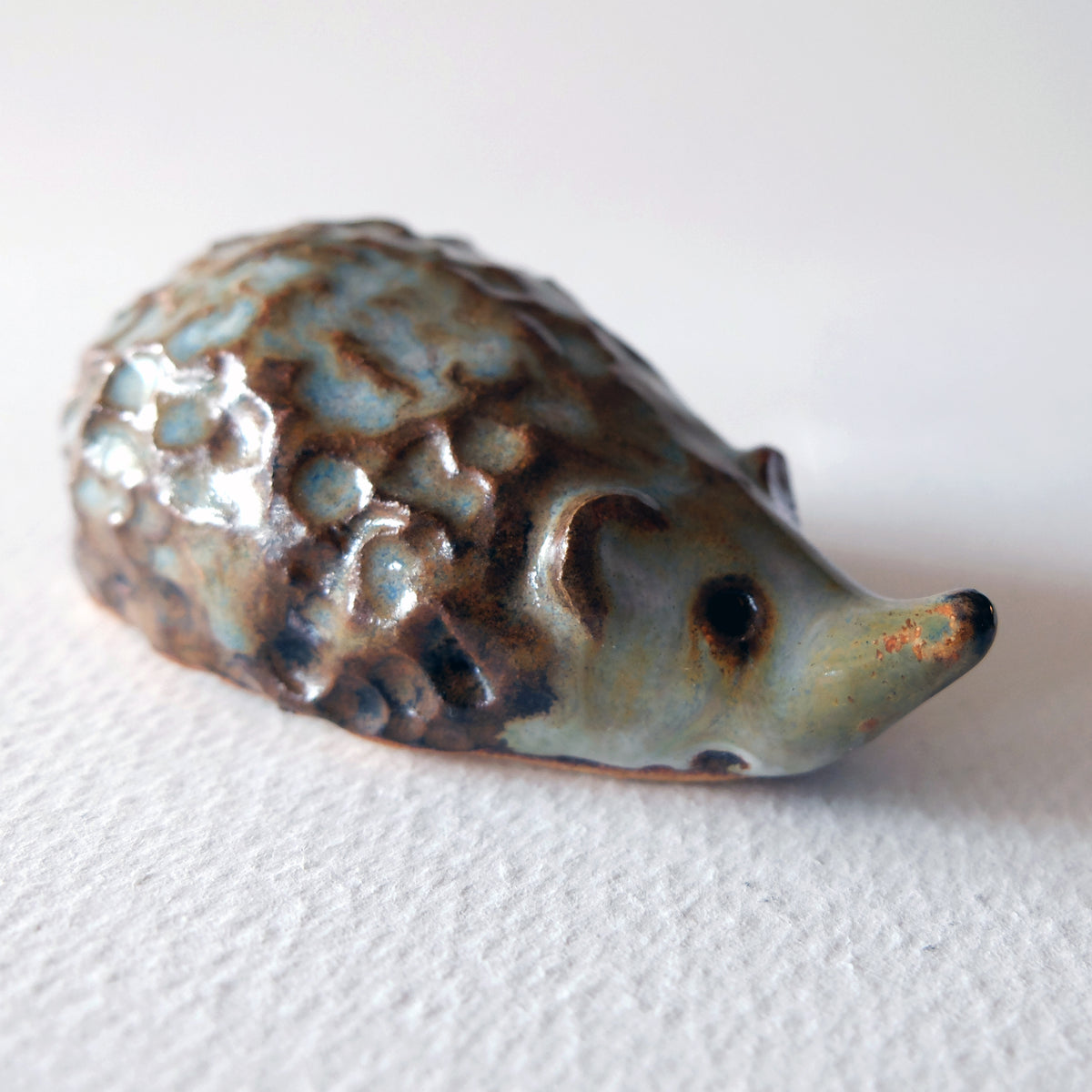Handcrafted ceramic hedgehog figurine with a long snout and knobby textured back in a mottled blue-brown glaze, sculpted by Nikolaj Jesper Cyon.