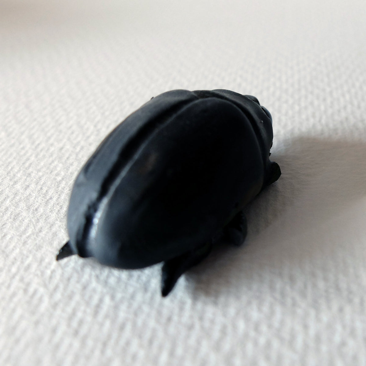 Handcrafted ceramic beetle figurine "The Midnight Beetle (#2)" in stoneware by Nikolaj Jesper Cyon. Rear perspective view highlighting the rounded carapace.