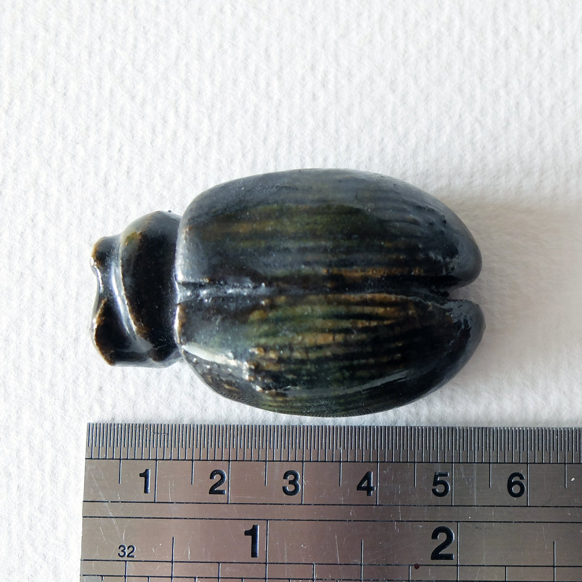 Handcrafted ceramic beetle figurine "The Obsidian Beetle (#4)" in stoneware by Nikolaj Jesper Cyon. Top-down view next to a metal ruler showing size scale.