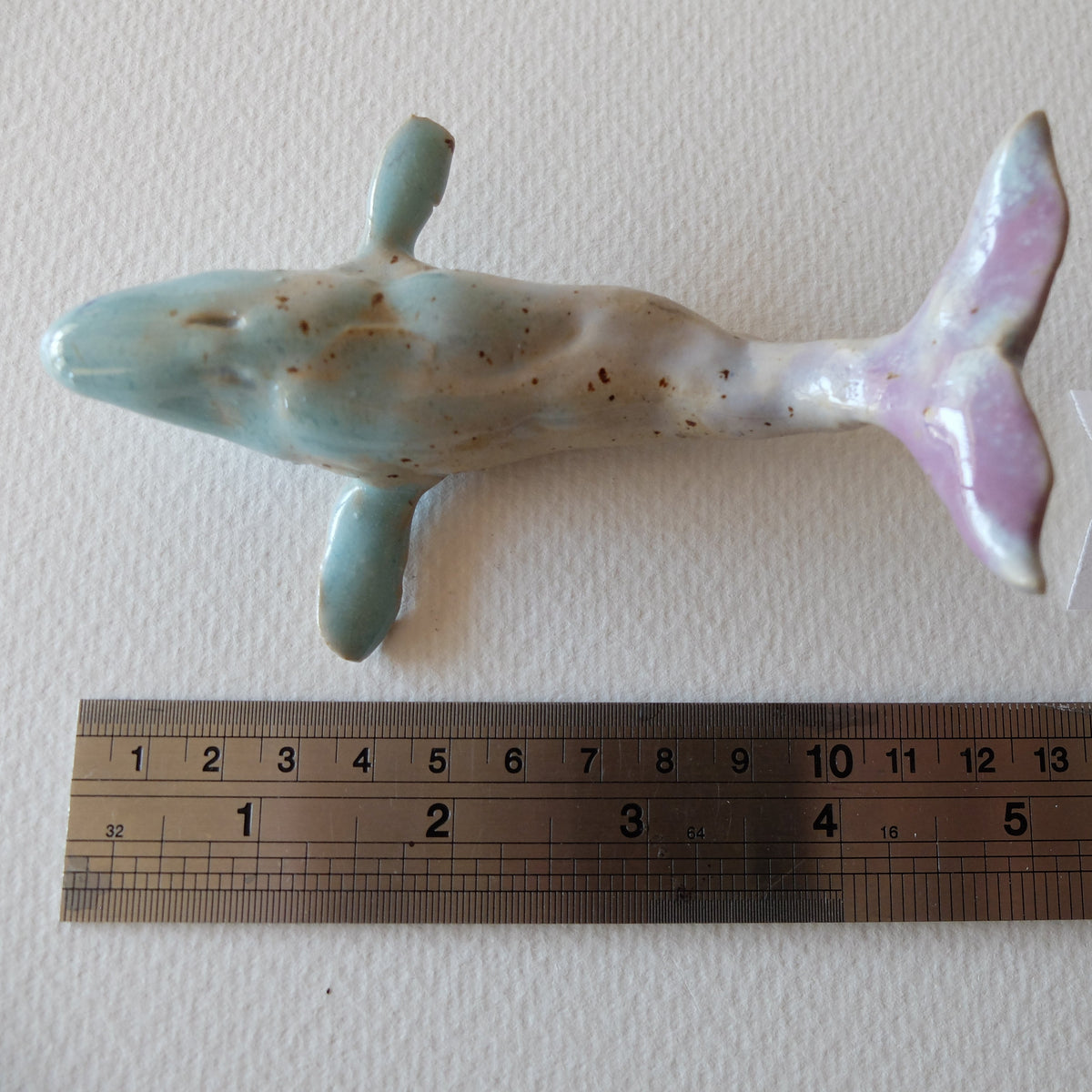 Handcrafted ceramic whale figurine "The Pastel Whale (#10)" in stoneware by Nikolaj Jesper Cyon. Top-down view next to a metal ruler showing size scale.