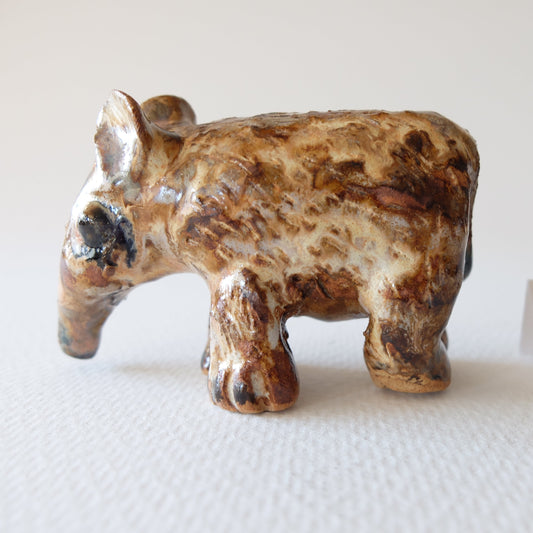 Handcrafted ceramic animal figurine "The Spotted Tapir (#7)" in stoneware by Nikolaj Jesper Cyon. Captured in a full side profile view, showing a long curved snout, large rounded ears, and four sturdy textured legs. Glazed with earthy brown, ochre, and dark spotted patterns on a rough stoneware body.