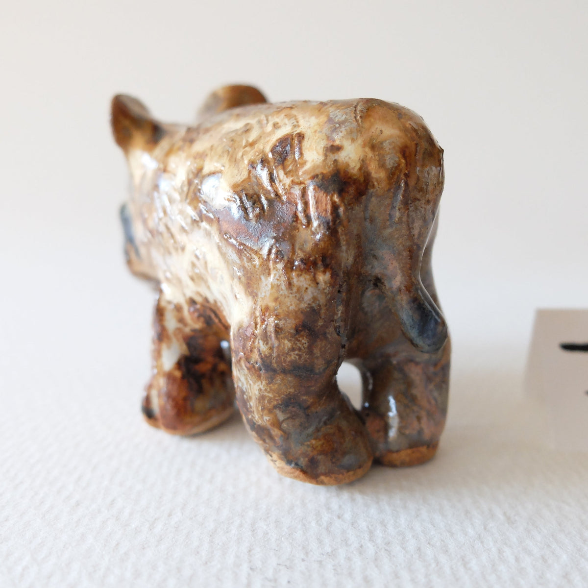 Handcrafted ceramic tapir figurine "The Spotted Tapir (#7)" in stoneware by Nikolaj Jesper Cyon. Rear perspective view showing its rounded body and glossy earthen glaze finish.