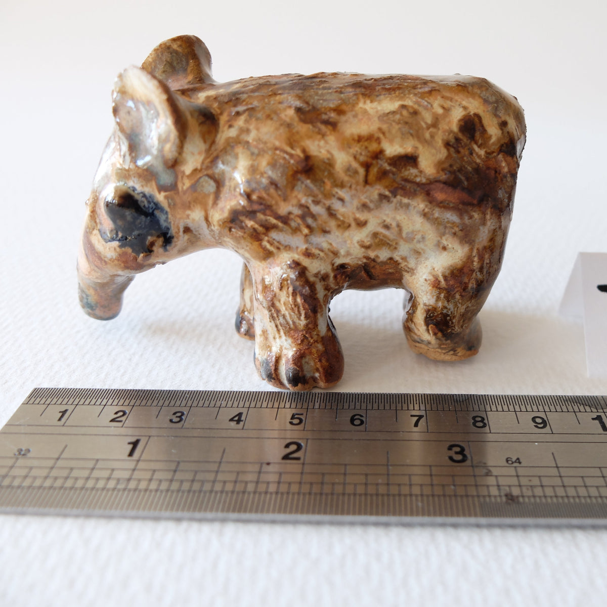 Handcrafted ceramic tapir figurine "The Spotted Tapir (#7)" in stoneware by Nikolaj Jesper Cyon. Side profile view next to a metal ruler showing size scale.