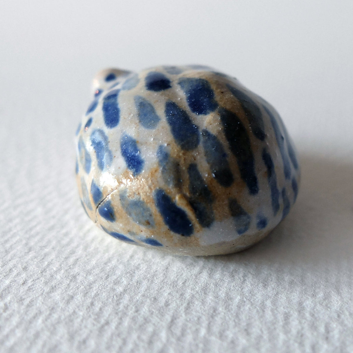 Handcrafted ceramic hedgehog figurine "The Striped Hedgehog (#3)" in stoneware by Nikolaj Jesper Cyon. Rear view showing the rounded back with dark blue and ochre speckled patterns on a light base.