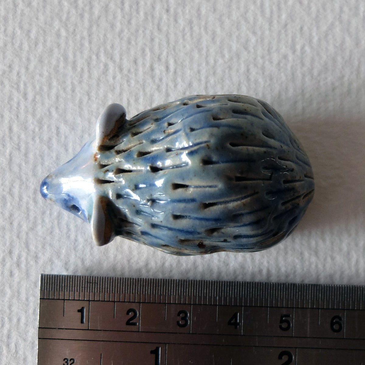 Handcrafted ceramic hedgehog figurine "The Timid Jade-Gazer (#1)" in stoneware by Nikolaj Jesper Cyon. Top view next to a ruler showing size scale.