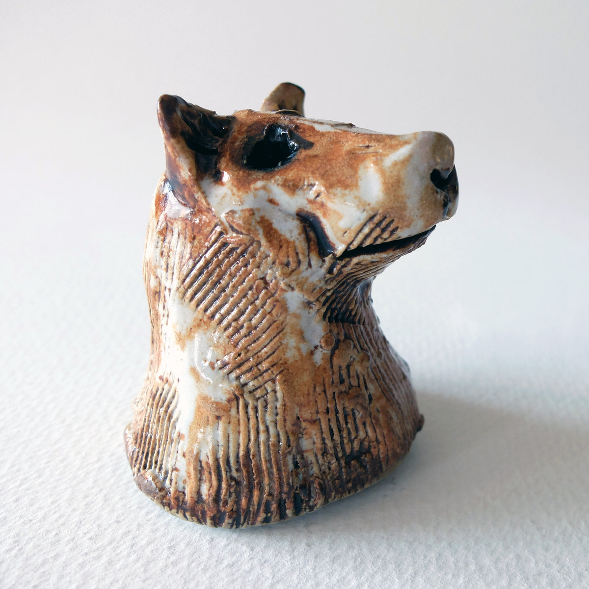 Handcrafted ceramic hound bust with textured fur and an expressive face in a glossy white, tan, and warm brown glaze, sculpted by Nikolaj Jesper Cyon.