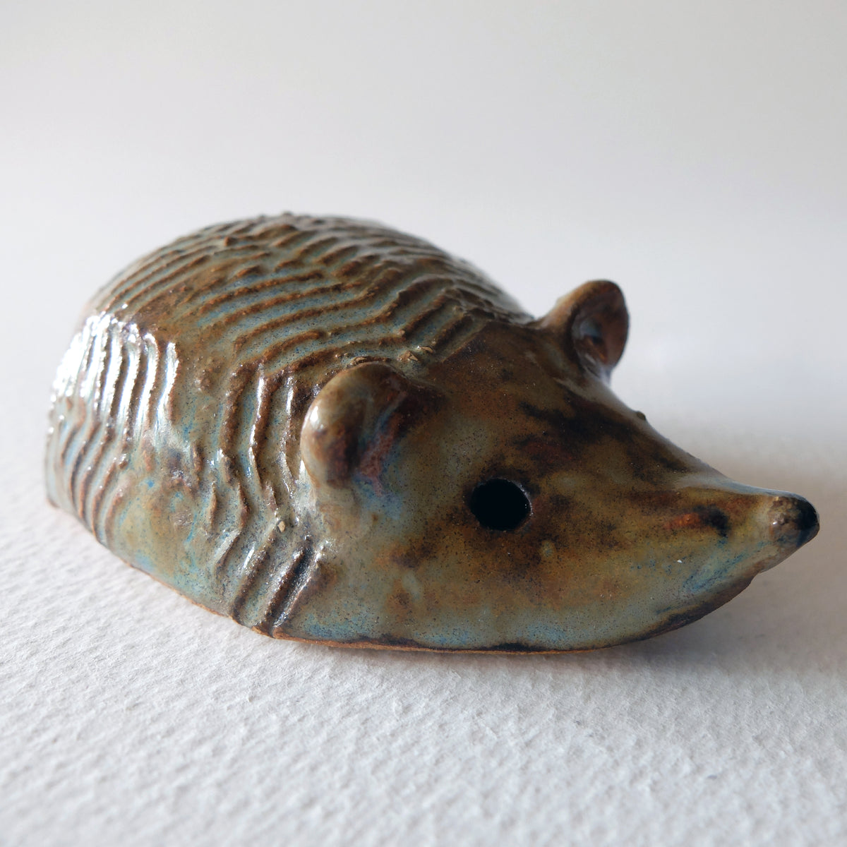 Handcrafted ceramic hedgehog figurine with carved zigzag ridge patterns across its back in a blue-grey and earthy brown glaze, sculpted by Nikolaj Jesper Cyon.